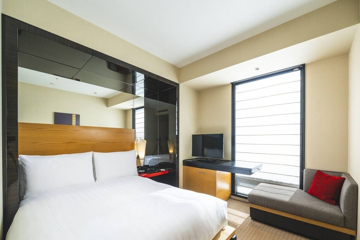 Ein Hotelzimmer mit Bett, Schreibtisch, Fernseher, Sofa und einem großen Fenster.