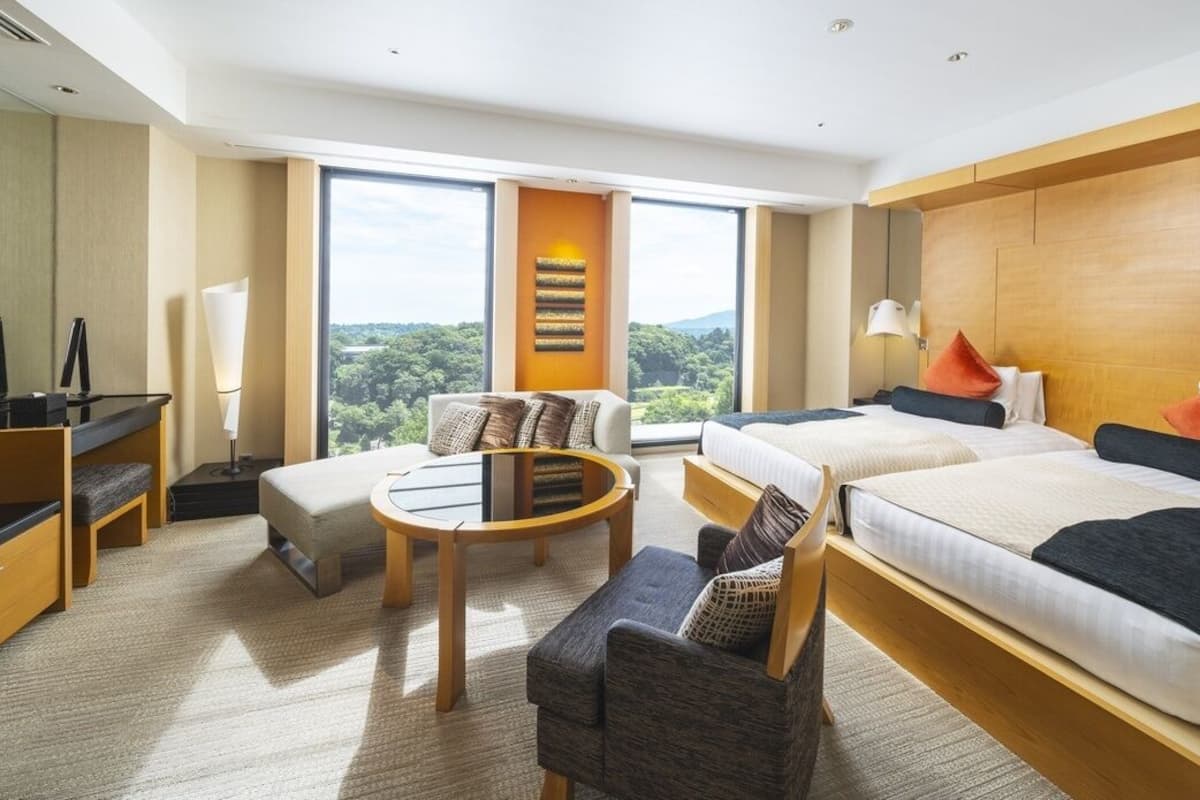 Ein Hotelzimmer mit zwei Betten, einer Schlafcouch, einem kleinen Tisch und einem Fernseher.