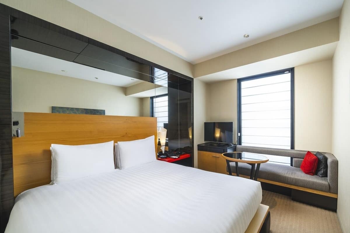 Ein Hotelzimmer mit einem großen Bett, einer Schlafcouch, einem Fernseher und einem Fenster.