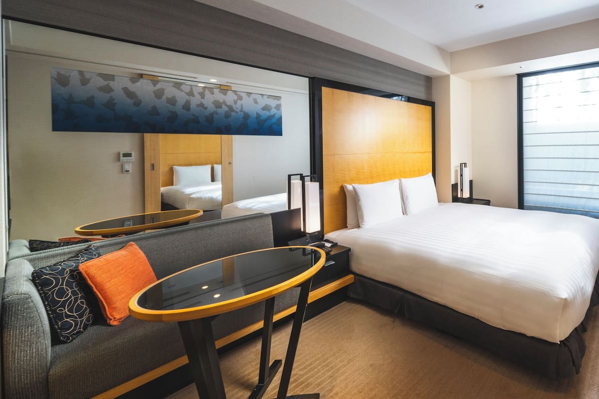 Ein Hotelzimmer mit Bett, einer Couch, einem kleinen Tisch, einem Spiegel und einem großen Fenster.