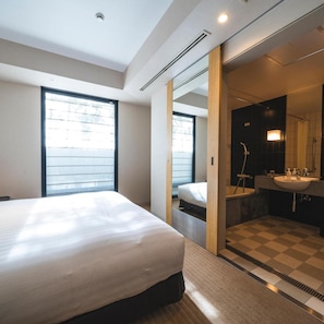 A modern hotel room with a large bed, a bathroom with a sink and mirror, and a view through a large window. - Koko Hotel Premier Kanazawa Korinbo (Kanazawa)