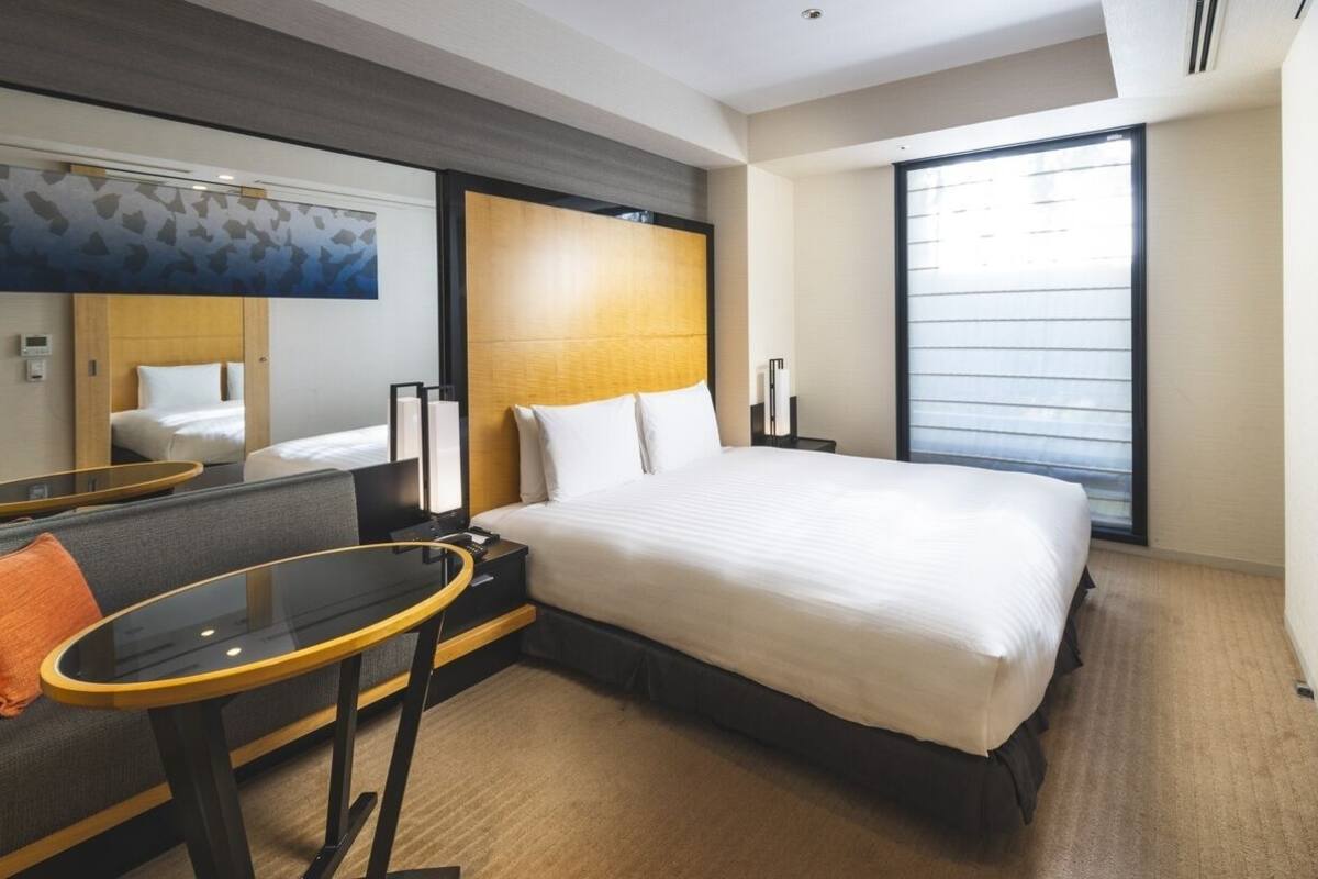 Ein Hotelzimmer mit einem Bett, einem Sofa, einem kleinen Tisch, einem Spiegel und einem großen Fenster.