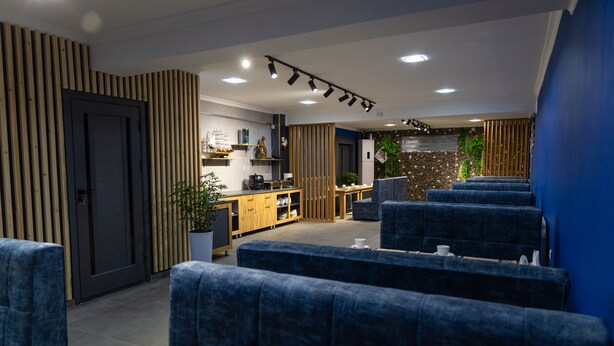 A modern waiting area with blue upholstered seating, a reception desk, and a kitchen in the background. - THE TIME HOTEL (Tashkent)