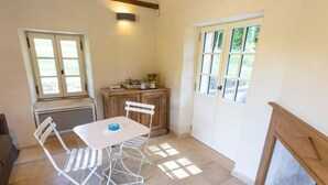 Una habitación con una mesa y sillas blancas, un armario de madera, una puerta con ventanas y una chimenea.