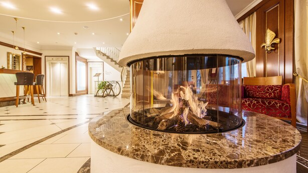 A lobby with a central fire feature, a staircase, and seating areas. - Hotel Dreiflüssehof Gästehaus (Passau)