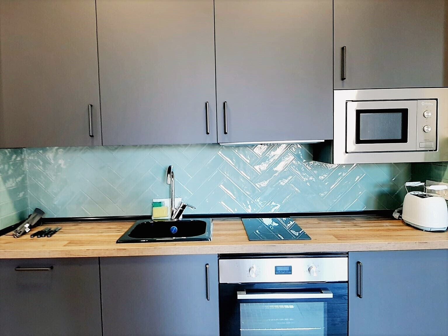 A kitchen with grey cabinets, a microwave, a toaster, and a dishwasher.