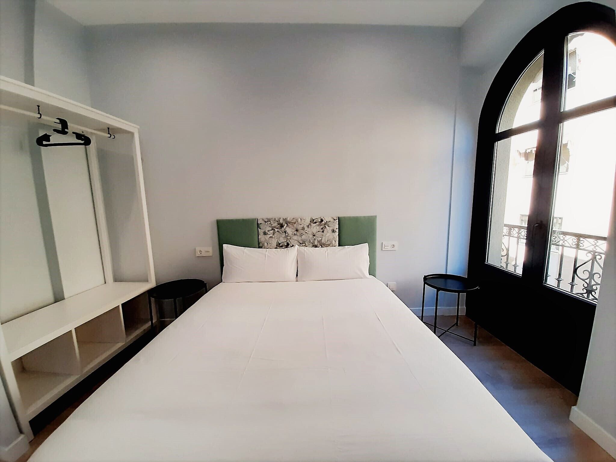 A bedroom with a bed, a wardrobe, a small table, and a window with a view.