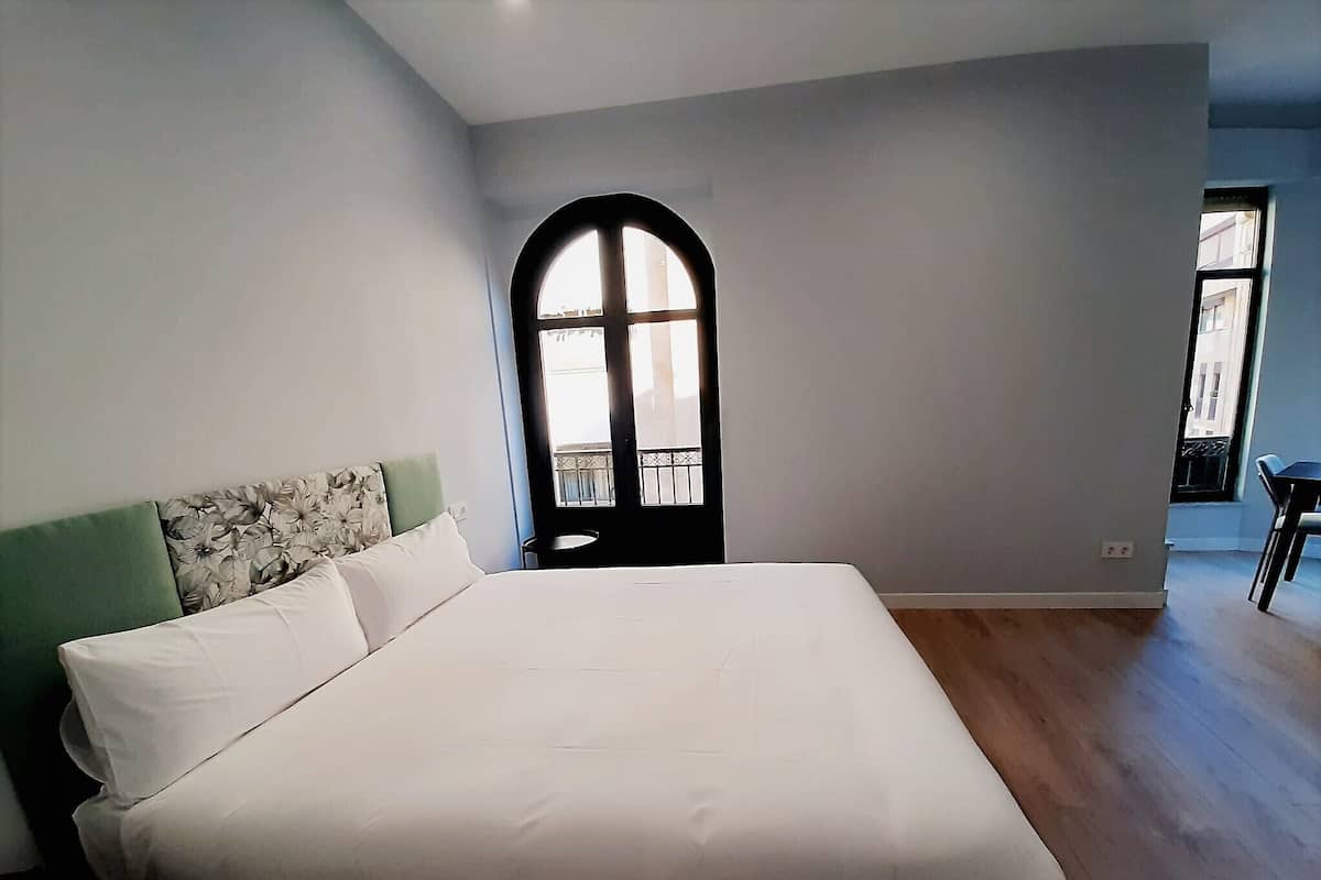 A bedroom with a large bed, a green headboard, and a window with a view of the outside.