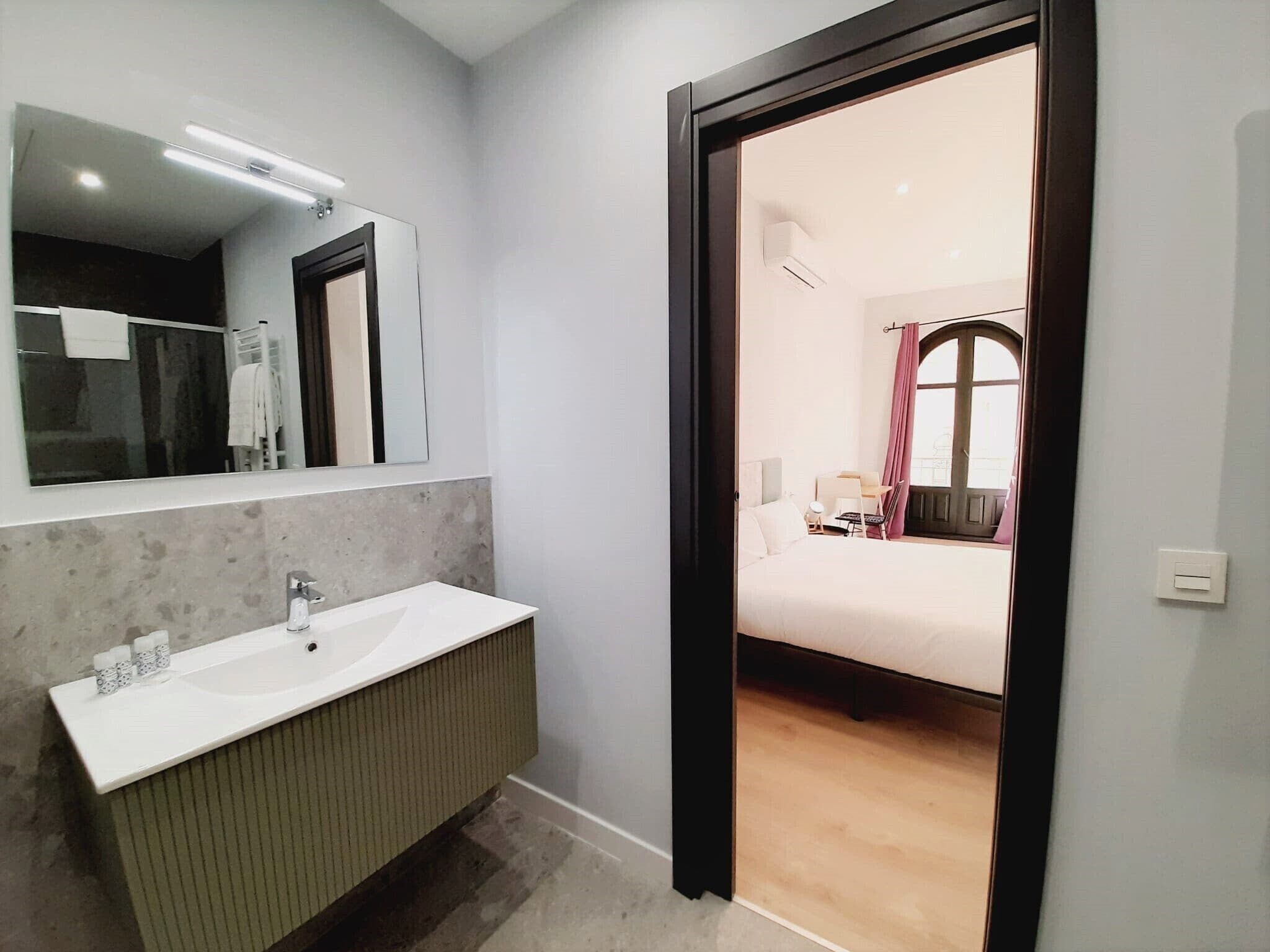 Un baño moderno con un espejo grande, un lavamanos blanco y un mueble de tocador de madera.