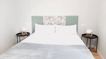 A neatly made bed with a white and grey bedspread, two bedside tables with lamps, and a wall with a floral pattern.