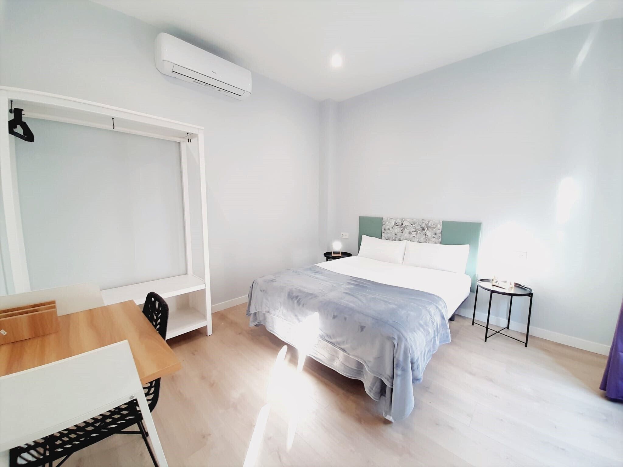 Un dormitorio minimalista con una cama, mesita de noche y una pequeña mesa con sillas.