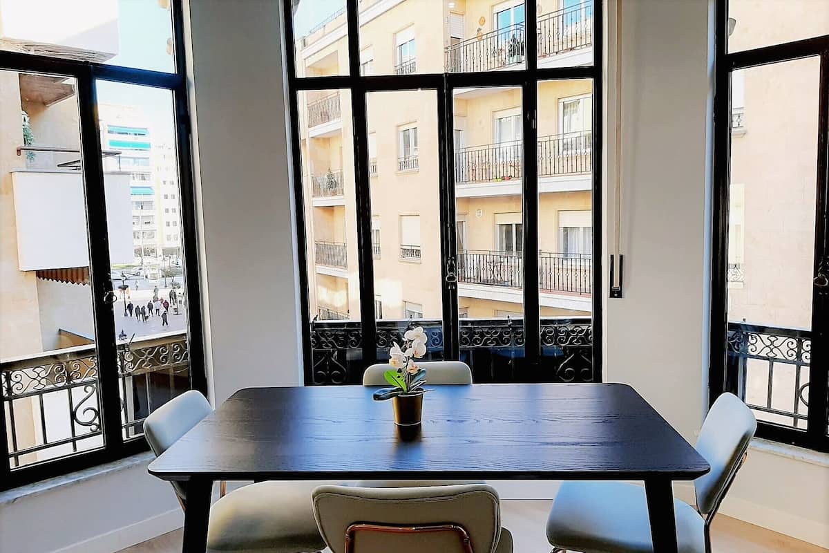 A dining area with a table and chairs, a potted plant, and large windows with balconies.