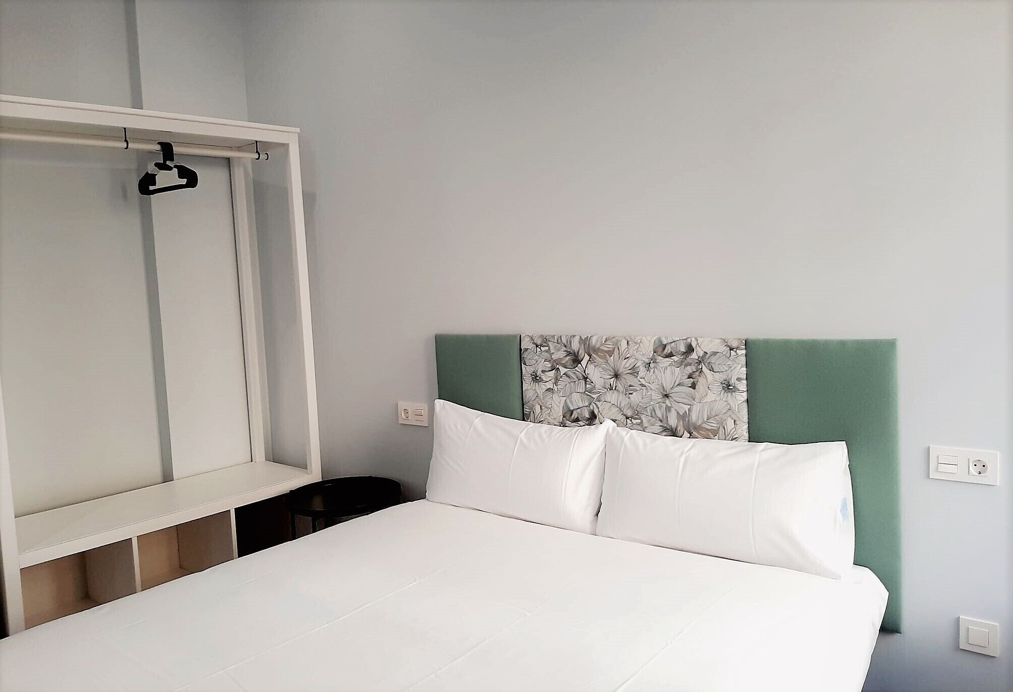 A bed with white bedding, a green headboard, and a floral-patterned wall panel.