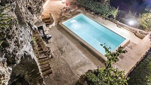 A swimming pool with a stone deck, surrounded by a rocky cliff and a small pavilion with a red umbrella. - Villa in the historical center with private garden, pool, spa and AC (Narni)