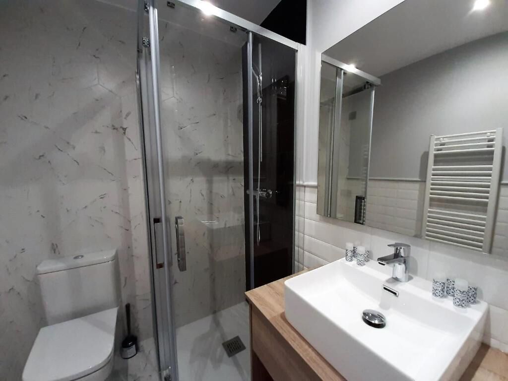 Un baño moderno con ducha de vidrio, un lavabo blanco con tocador de madera y un espejo sobre el lavabo.
