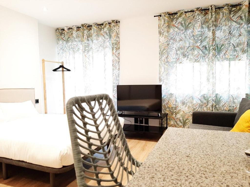 Une chambre d’hôtel avec un lit, un téléviseur posé sur un meuble, une chaise et des rideaux à motifs tropicaux.