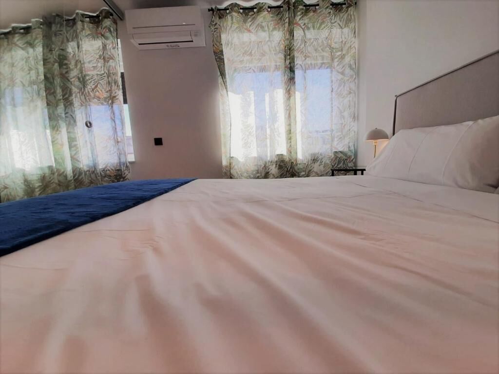 Habitació d'hotel amb un llit gran, una tauleta de nit i una finestra amb cortines.