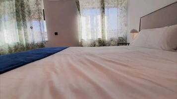 Habitació d'hotel amb un llit gran, una tauleta de nit i una finestra amb cortines.