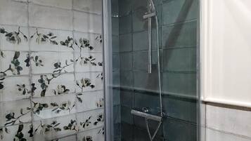 Ducha con puerta de vidrio y pared cubierta de azulejos con motivos florales.