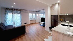 A modern living room with a sofa, a TV, and a kitchen area with a sink and cabinets. - Apartamentos Celestina by gaiarooms (Salamanca)