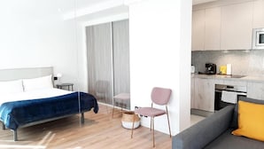 A modern hotel room with a bed, a grey sofa, a small kitchen area, and a dining table. - Apartamentos Celestina by gaiarooms (Salamanca)