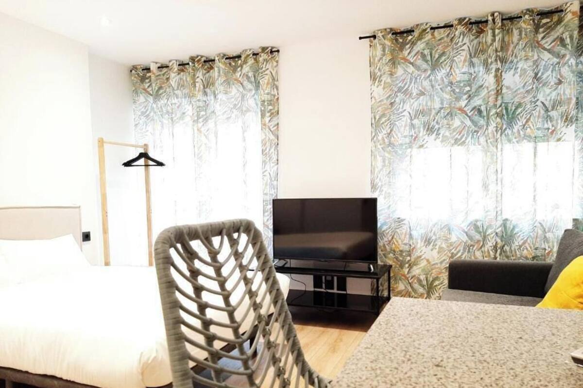 A hotel room with a bed, a TV, a chair, and curtains with a tropical pattern.
