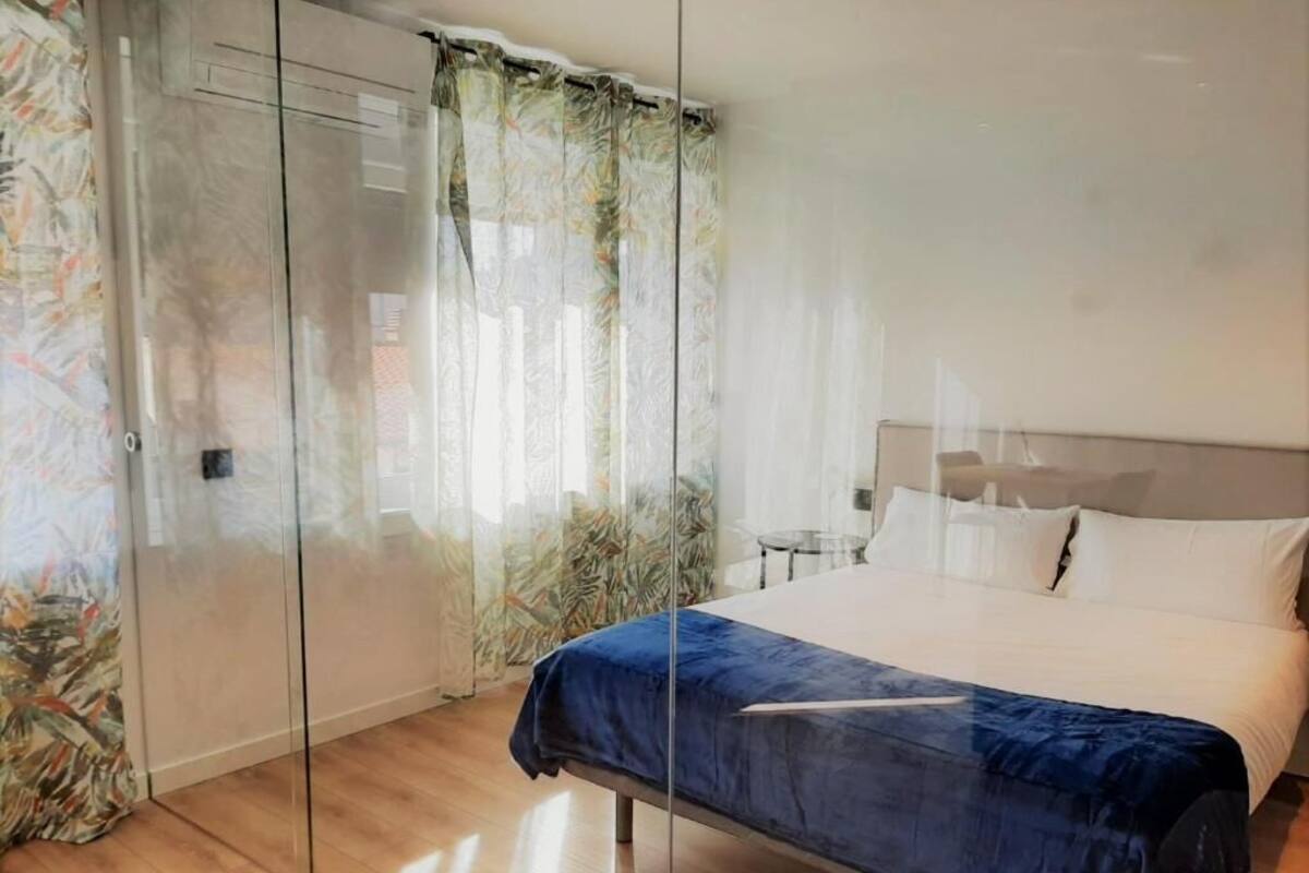 A bedroom with a bed, a glass partition, and a view of a cityscape.