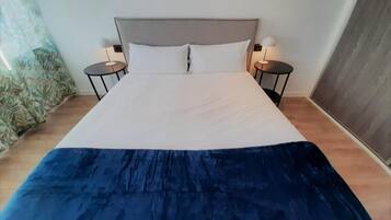 Una cama con cabecera gris, dos mesitas de noche con lámparas y una colcha azul.