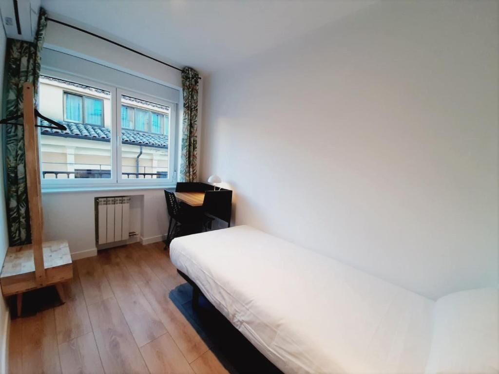 Ein kleines Hotelzimmer mit einem Bett, einem Schreibtisch und einem Fenster mit Blick auf ein Gebäude.