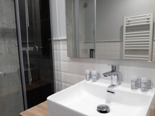 A bathroom with a white sink, a mirror, and a glass shower enclosure. - Apartamentos Celestina by gaiarooms (Salamanca)