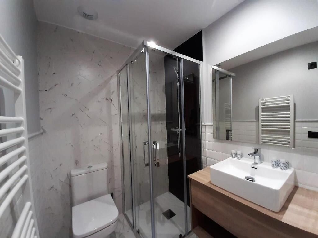 Un baño moderno con ducha de vidrio, inodoro blanco y tocador de madera con lavabo blanco.