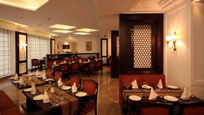 Zona pranzo di un hotel con diversi tavoli apparecchiati per gli ospiti, caratterizzata da varie disposizioni di posti a sedere e un pannello decorativo con motivo geometrico.