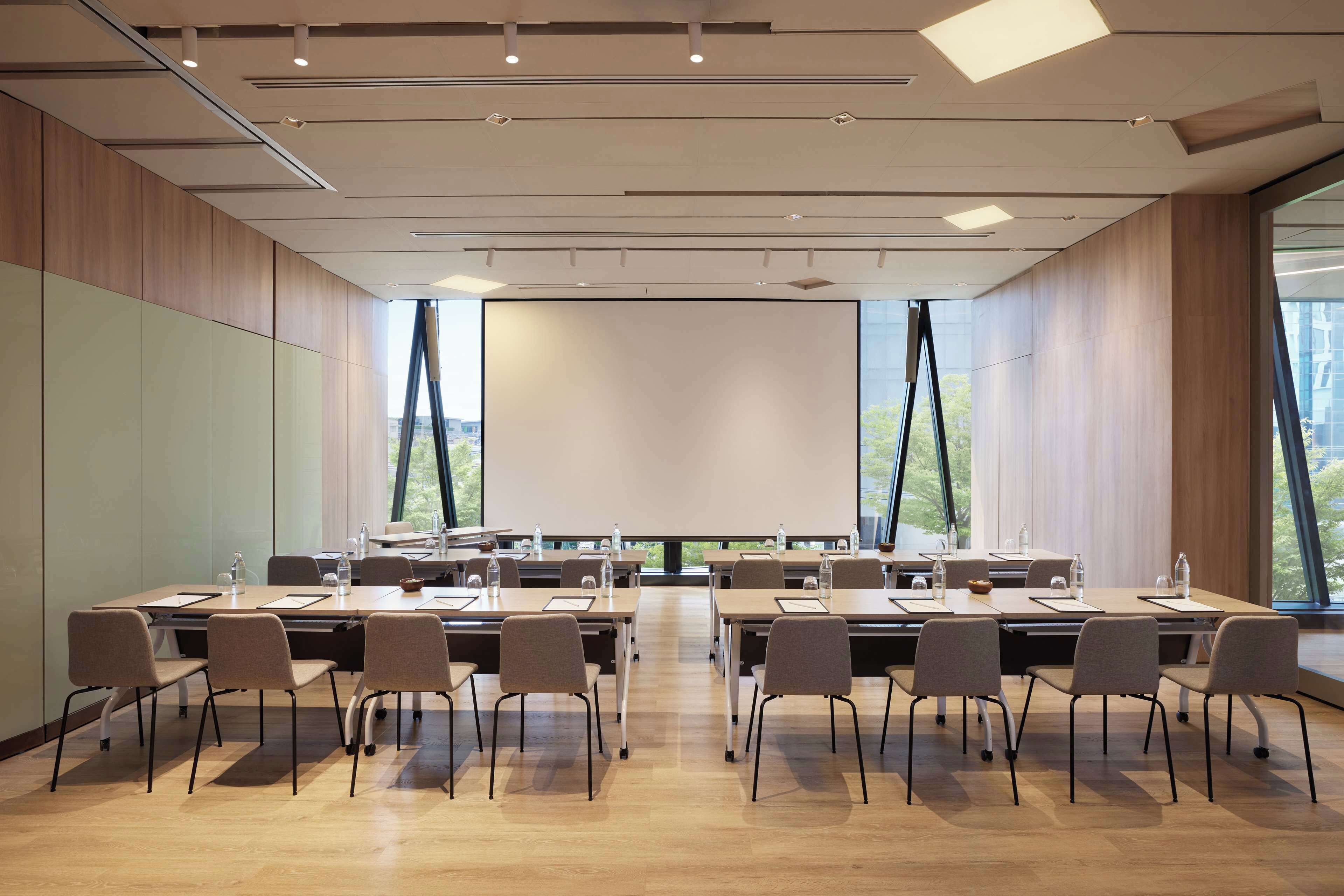 A conference room with a long table, chairs, and a projector screen.