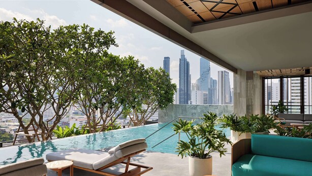 A rooftop infinity pool with lounge chairs and a sofa, surrounded by potted plants and overlooking a cityscape. - Dusitd2 Samyan Bangkok (Bangkok)