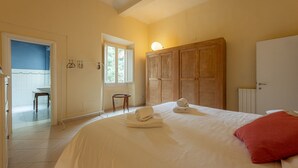 A bedroom with a bed, a red pillow, a wooden wardrobe, and a small table with towels.