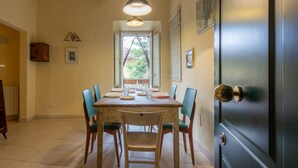 A dining area with a wooden table set for four, surrounded by six chairs, a hanging light fixture, and a door with a brass handle.