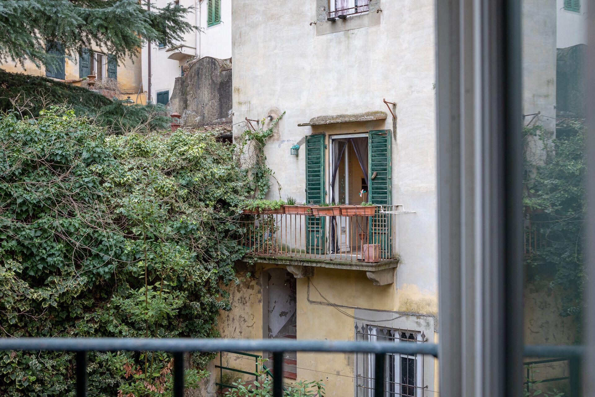Ein Balkon mit schmiedeeisernem Geländer, ein Fenster mit grünen Rollläden und ein Gebäude mit strukturierter Wand.