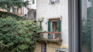 A balcony with a wrought iron railing, a window with green shutters, and a building with a textured wall.