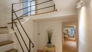 A staircase with a metal railing, a wooden table with a plant, and a hallway leading to a living area.