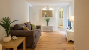 A living room with a sofa, a small table, a potted plant, and a TV stand.