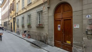 A street with a building featuring a large wooden door, metal bars on windows, and a sign indicating a private entrance.