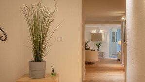A hallway with a potted plant on a wooden console table, a mirror on the wall, and a light fixture.