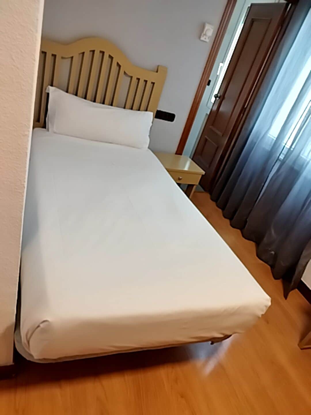 A single bed with a wooden headboard in a room with a wooden floor.