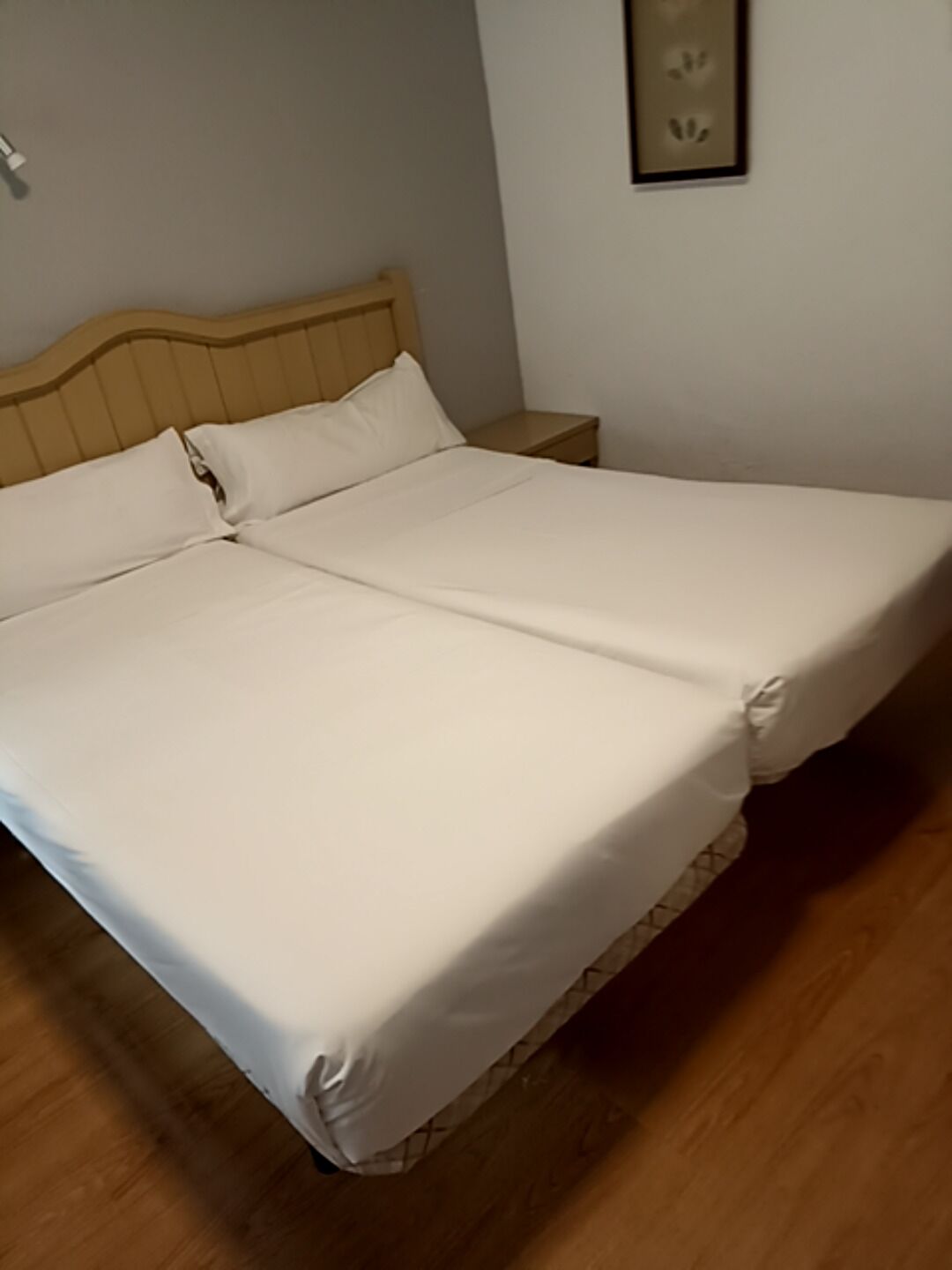 Uma cama de casal com roupa de cama branca em um quarto com piso de madeira e cabeceira de madeira.