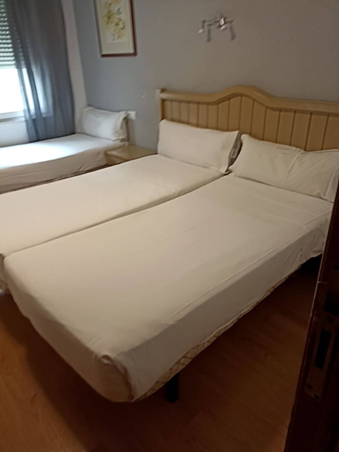 Habitación de hotel con dos camas individuales, cabeceros de madera y una mesita de noche pequeña.