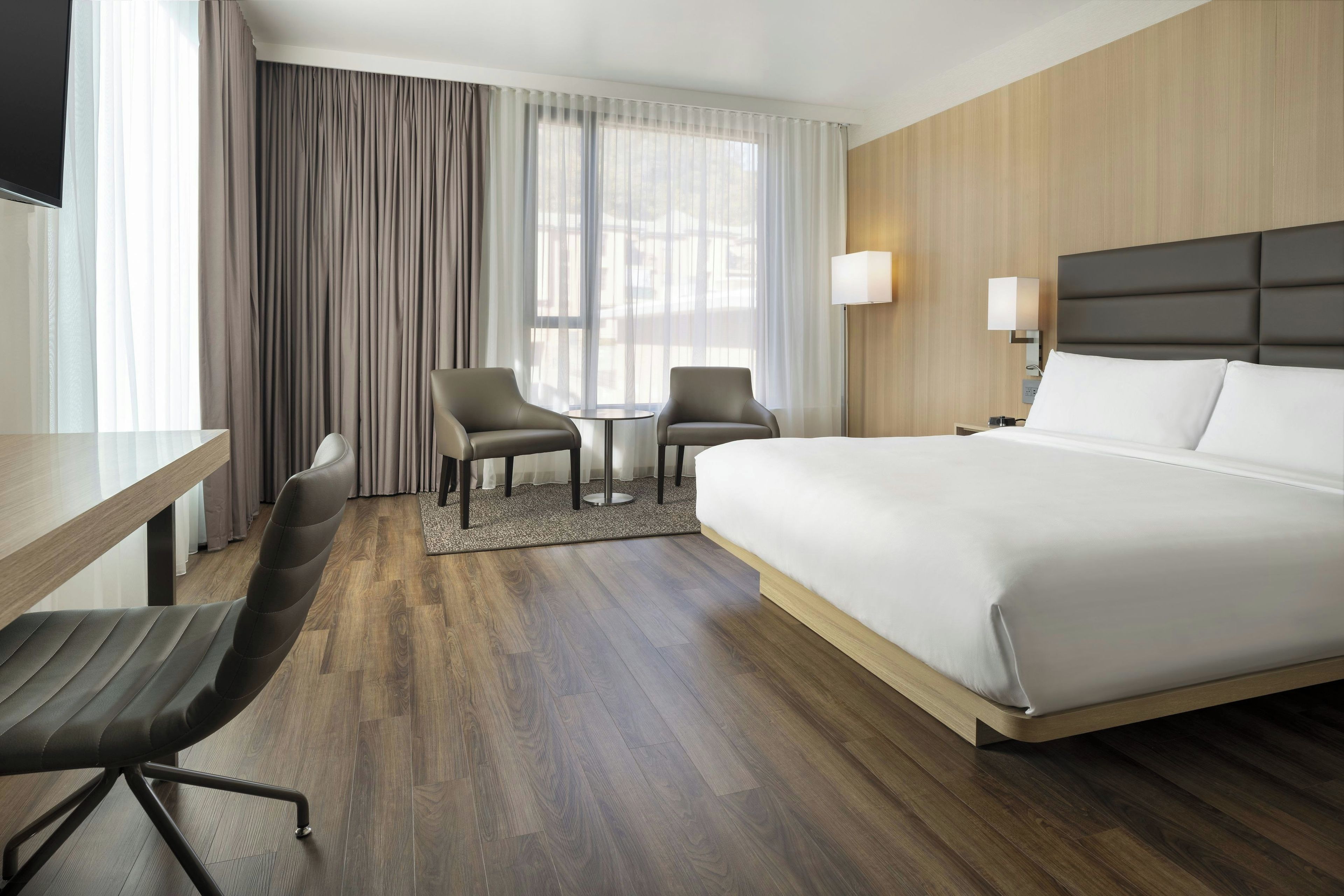 A hotel room with a large bed, two armchairs, a small table, and a desk.
