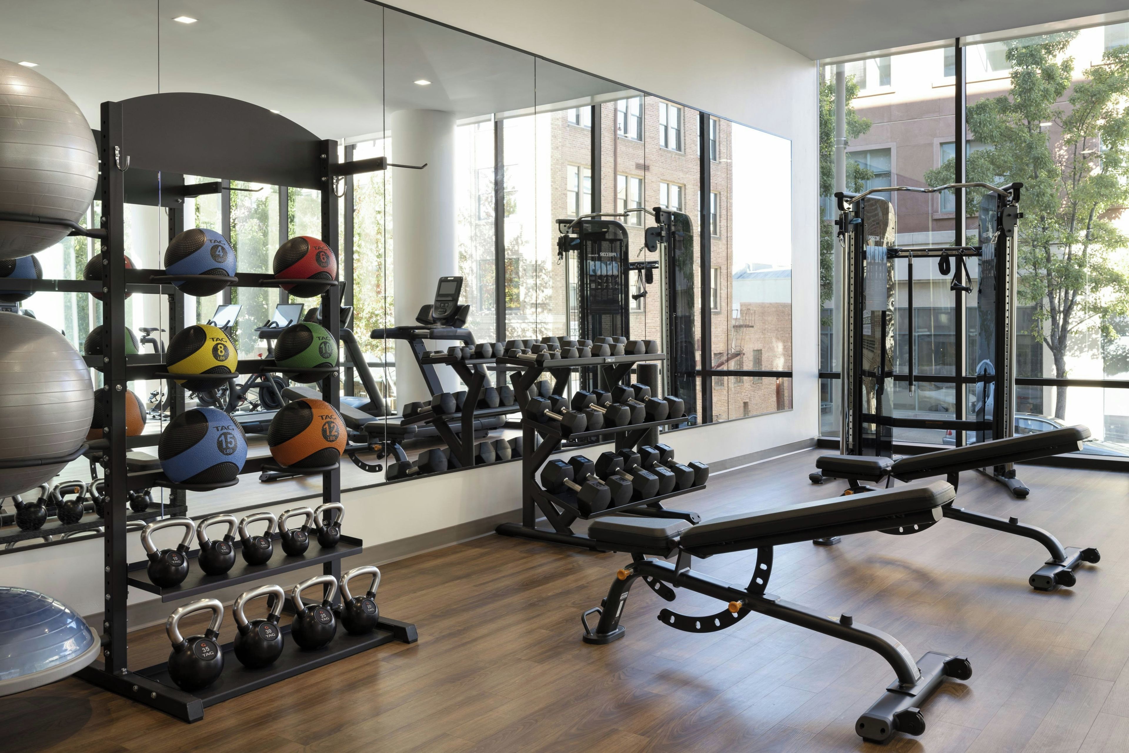 Un gimnasio con equipamiento de ejercicio, un espejo grande y amplias ventanas.