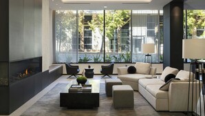 A modern living room with a fireplace, comfortable seating, and large windows offering a view of the outdoors. - AC Hotel San Rafael Downtown (San Rafael)