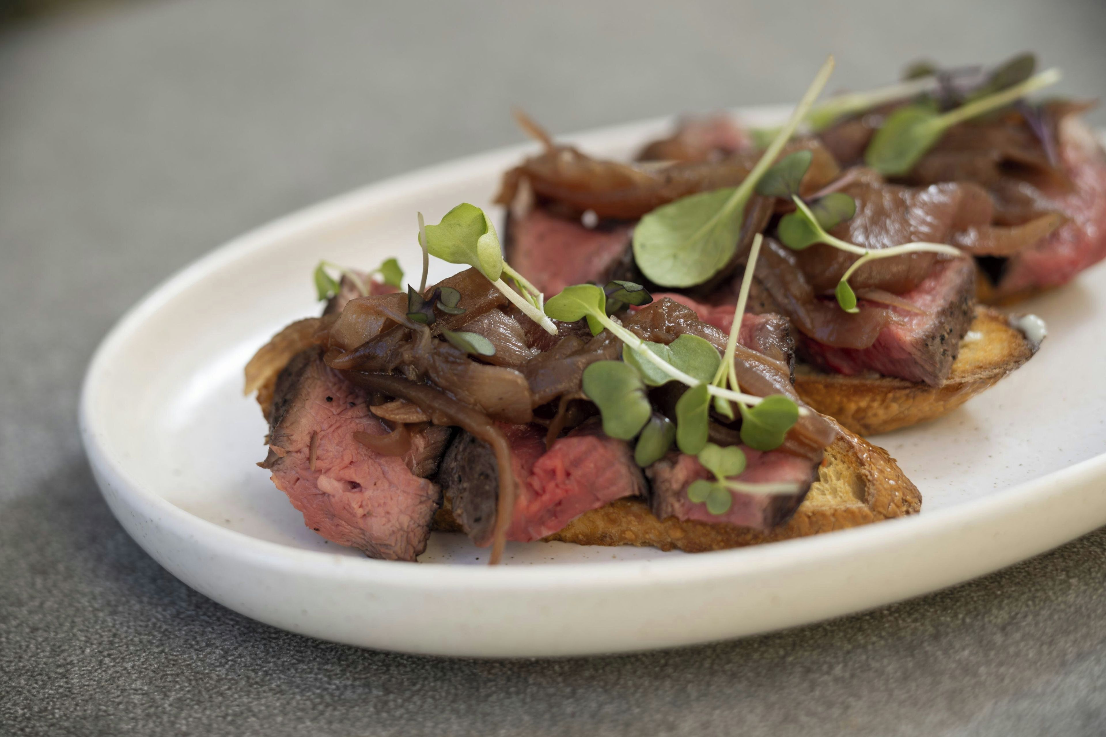A plate of food with sliced meat and greens on a white plate.