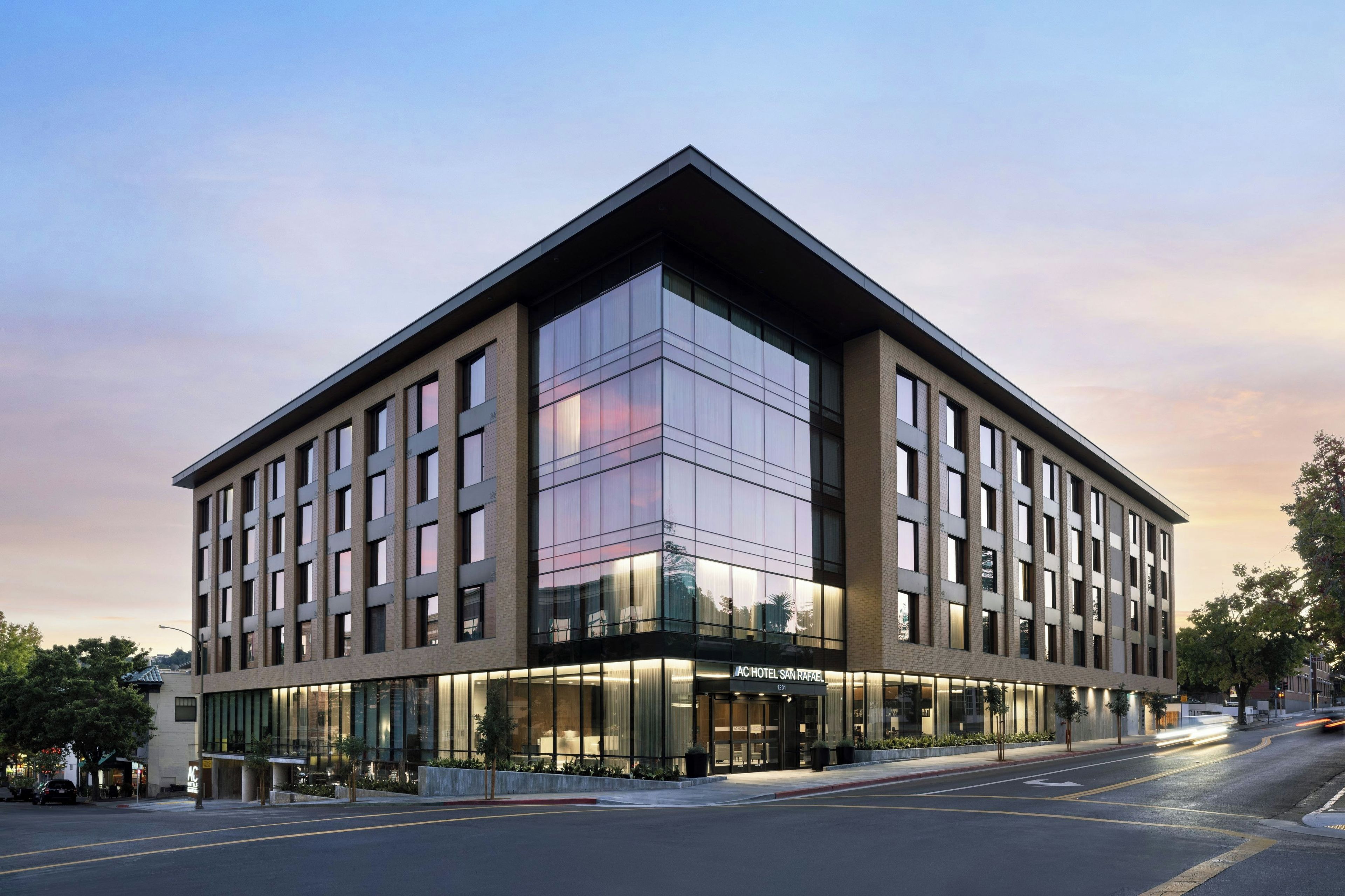 A modern hotel with a prominent glass facade, a flat roof, and a corner entrance.